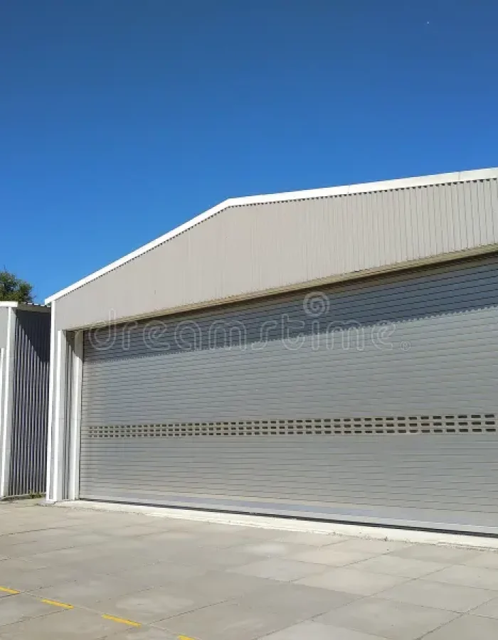 exterior-two-metal-hangar-storage-under-blue-sky-side-view-garages-closed-rolling-doors-concrete-blocked-flow-135705253